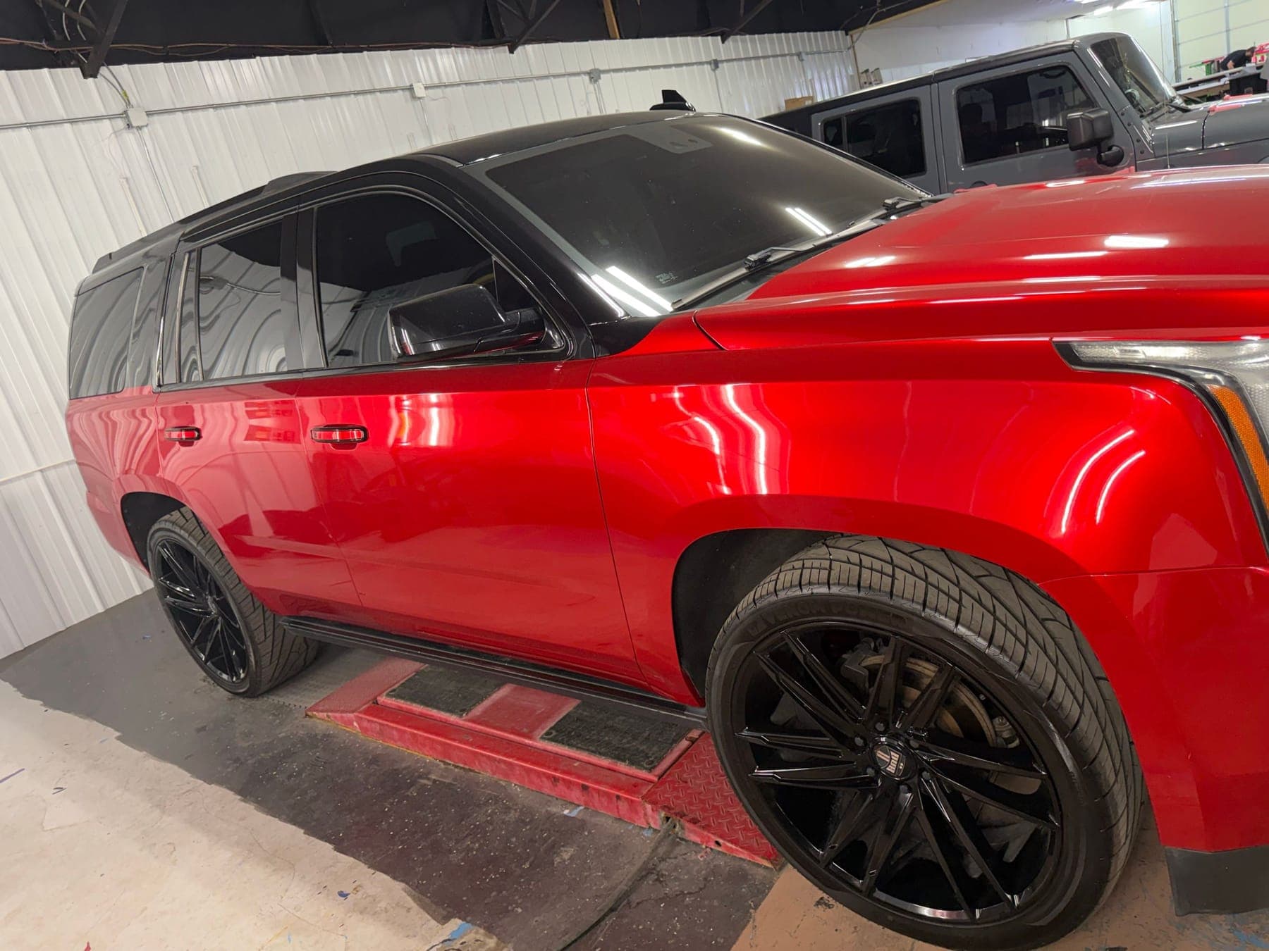 Shop lights reflected in the red paint of a GMC SUV on the indoor lift