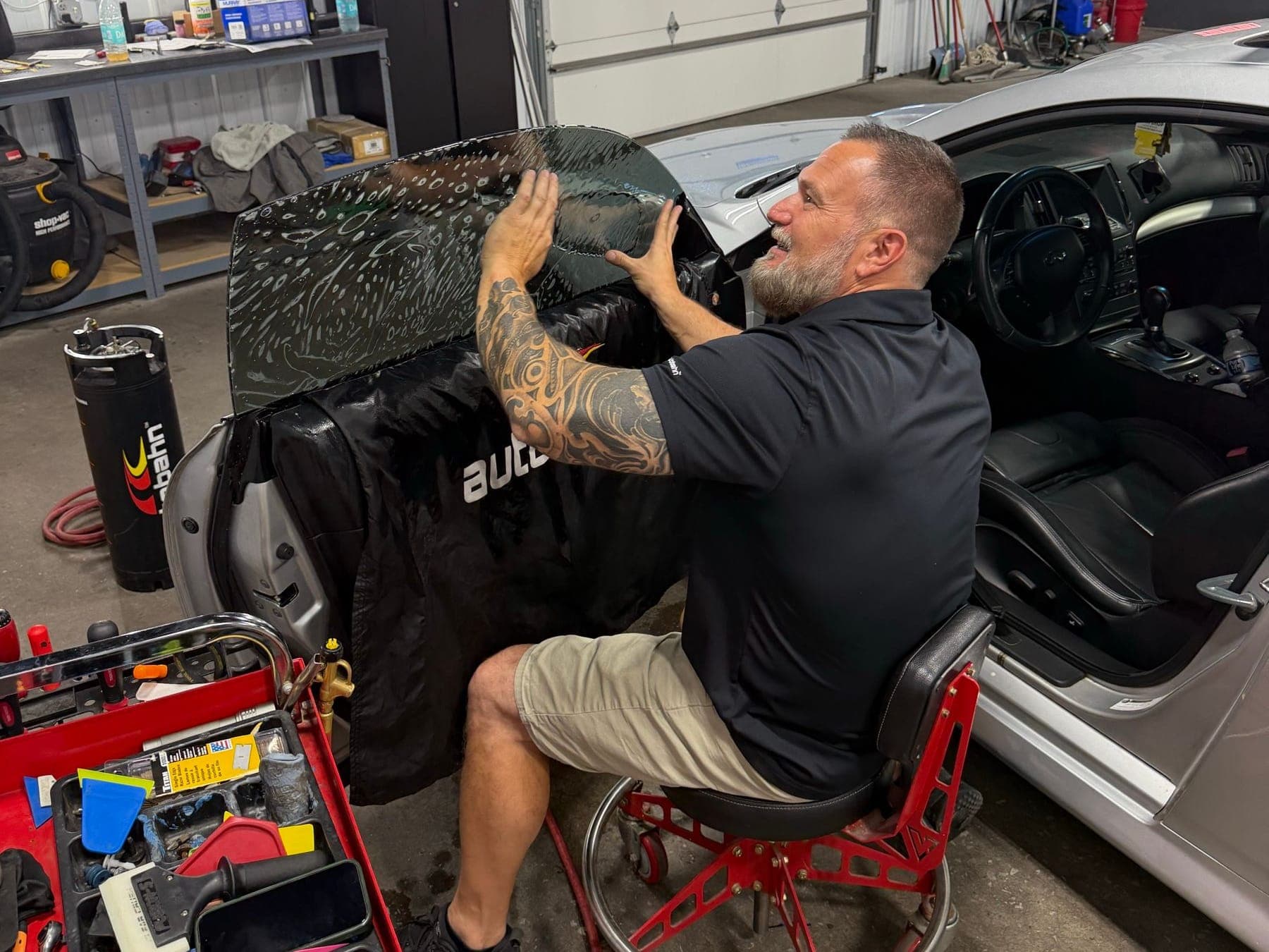 Technician fitting window film to a silver coupe in the Ironwood Motorsports tint bay
