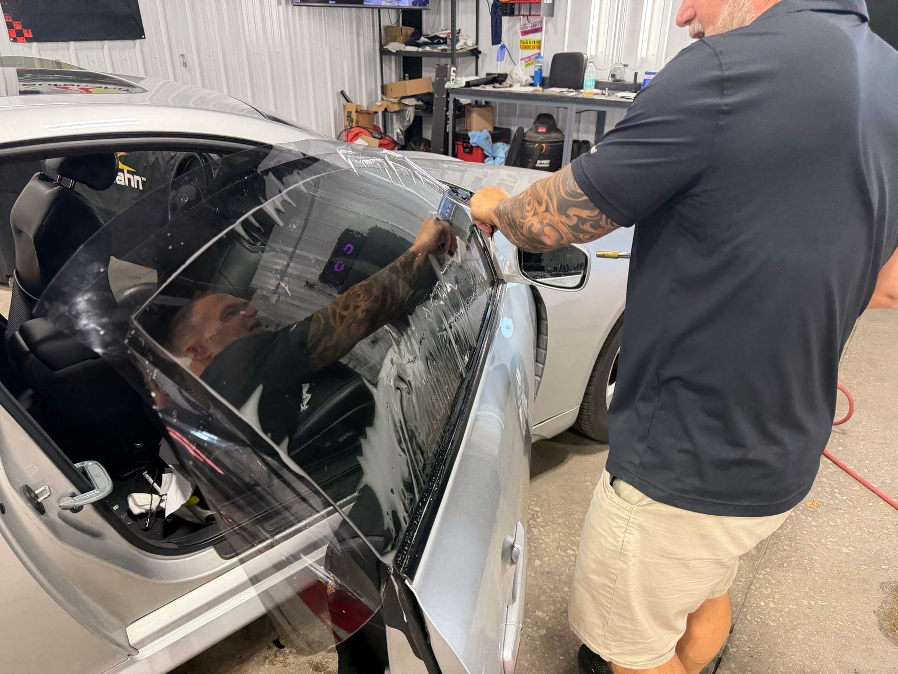 Technician positioning wet tint film on the side window of a silver coupe